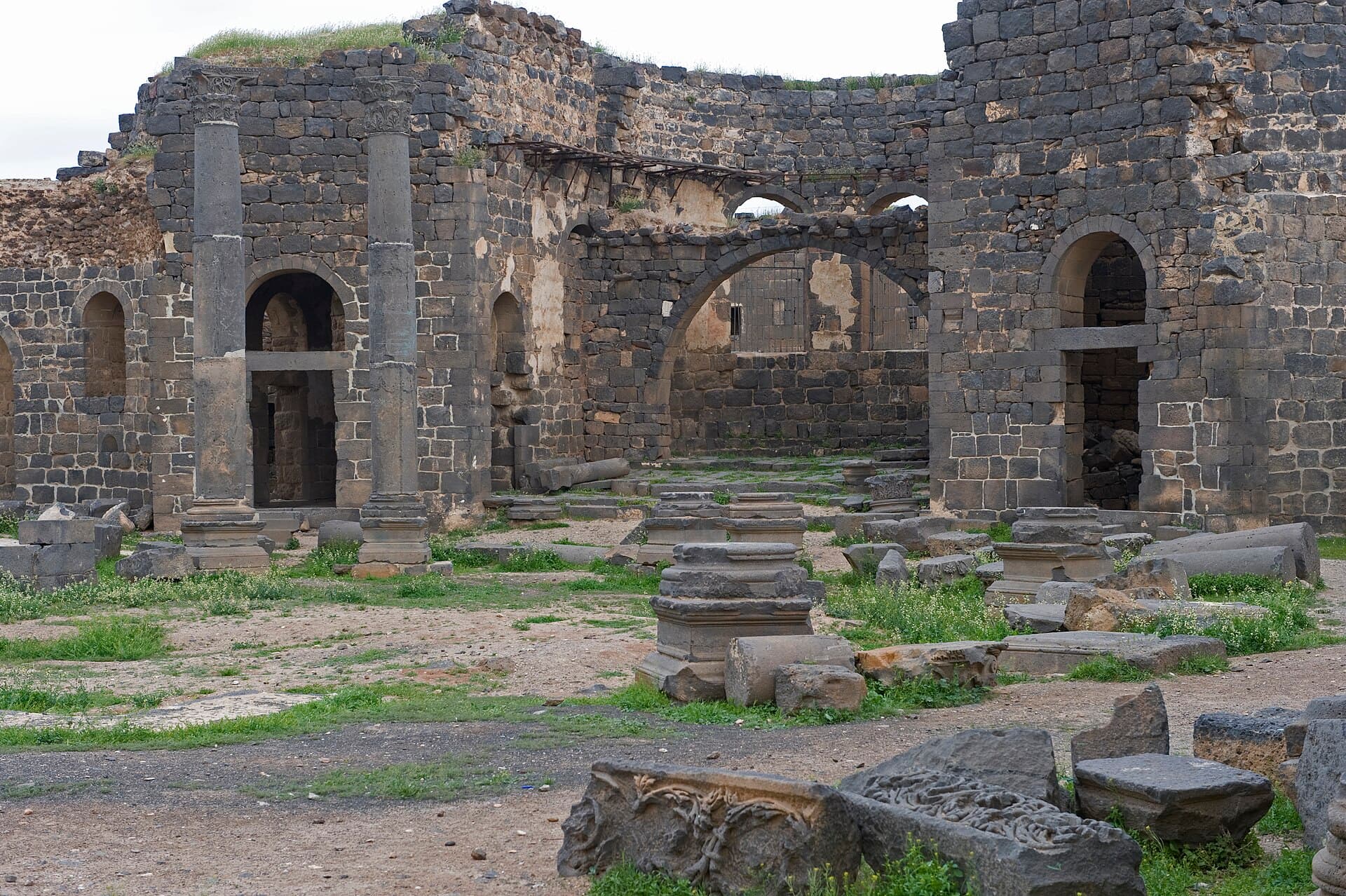 Busra Katedrali'nin bazalt duvarları, devrilmiş sütun kaideleri ve oymalı taş parçaları
