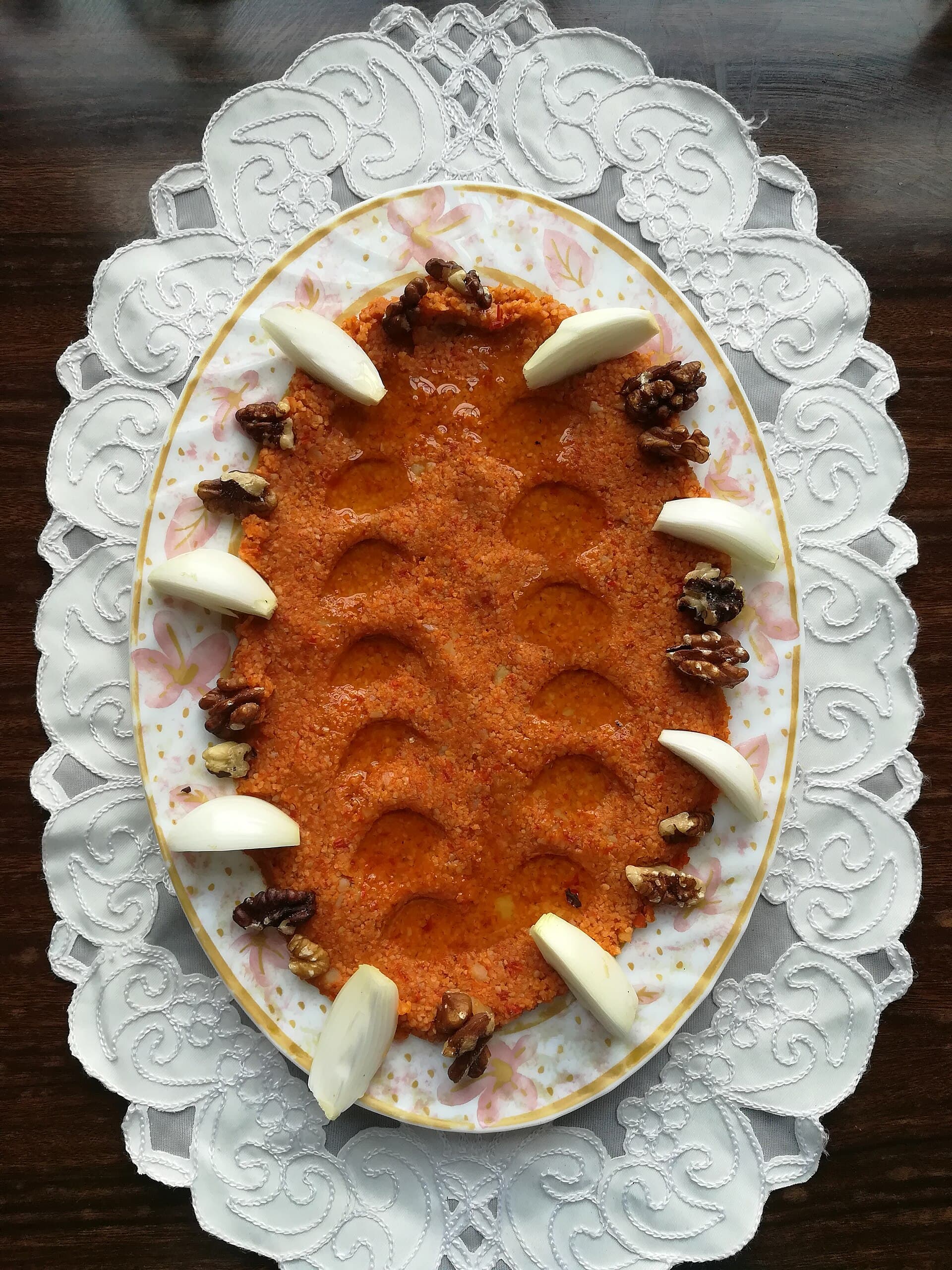 Çiğ kibbe oval tabakta yayılmış; kenarında soğan dilimleri ve ceviz, çukurlarında zeytinyağı