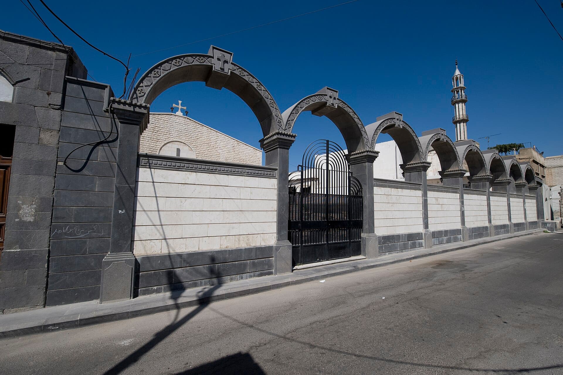 Mar Elian Kilisesi'nin sokak duvarı: siyah bazalt ve beyaz taşla örülmüş kemer dizisi, tepelerinde haç kabartmaları