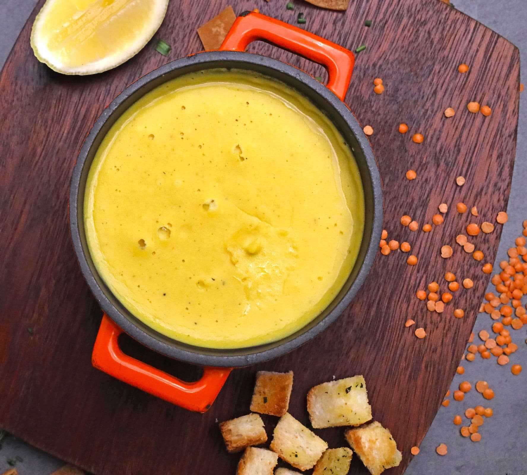 Pürüzsüz kırmızı mercimek çorbası; yanında limon, kızarmış ekmek küpleri ve kuru mercimek