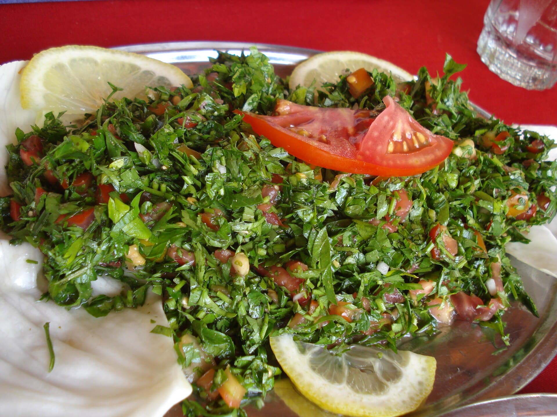Maydanoz, domates ve bulgurla hazırlanmış tebbule; yanında limon ve lahana yaprakları