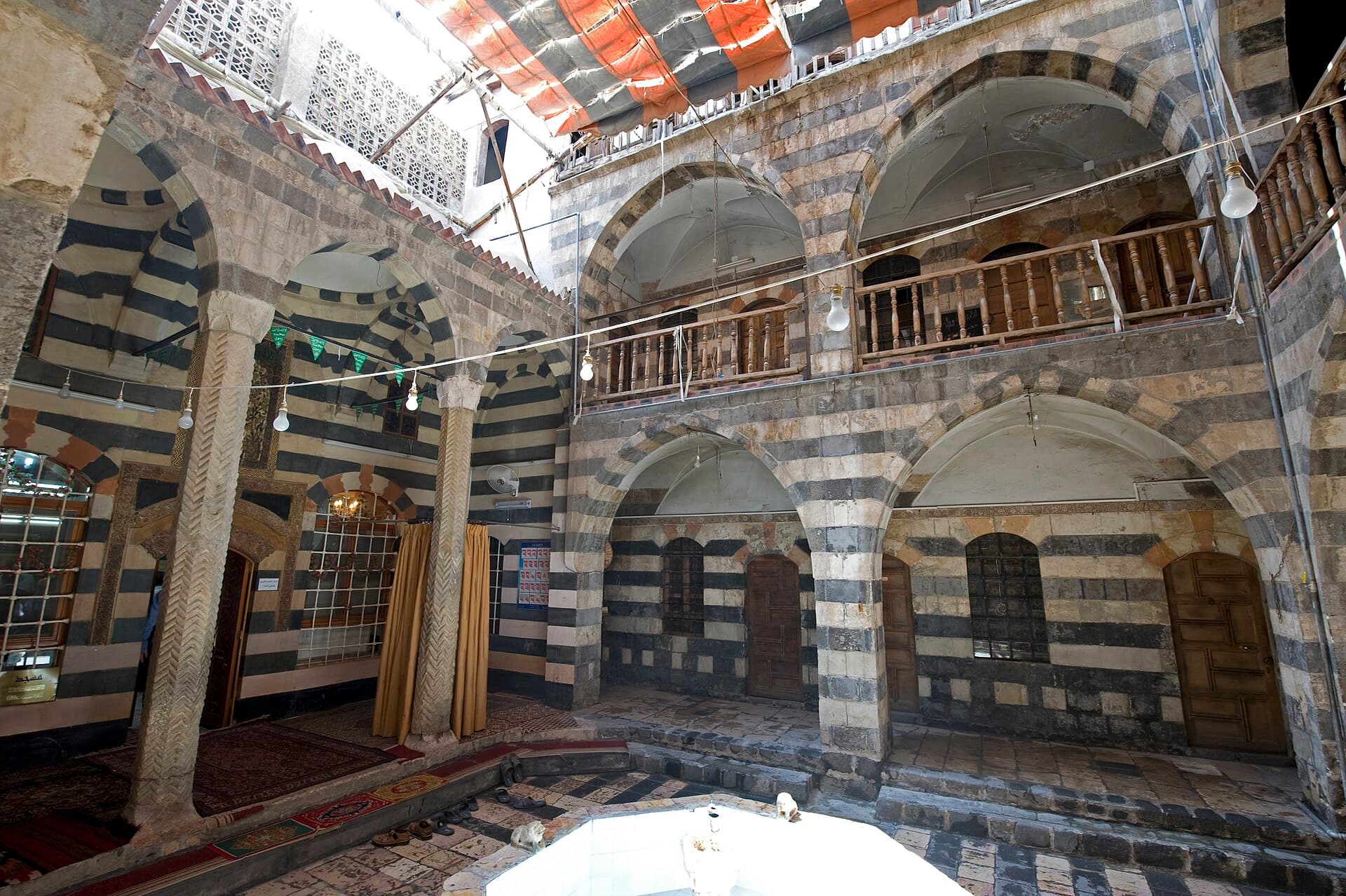 Abdullah Paşa el-Azm Medresesi'nin avlusu: ortada fıskiye, çevresinde siyah-beyaz almaşık taşla örülmüş iki kat revak ve üst galerinin ahşap korkuluğu