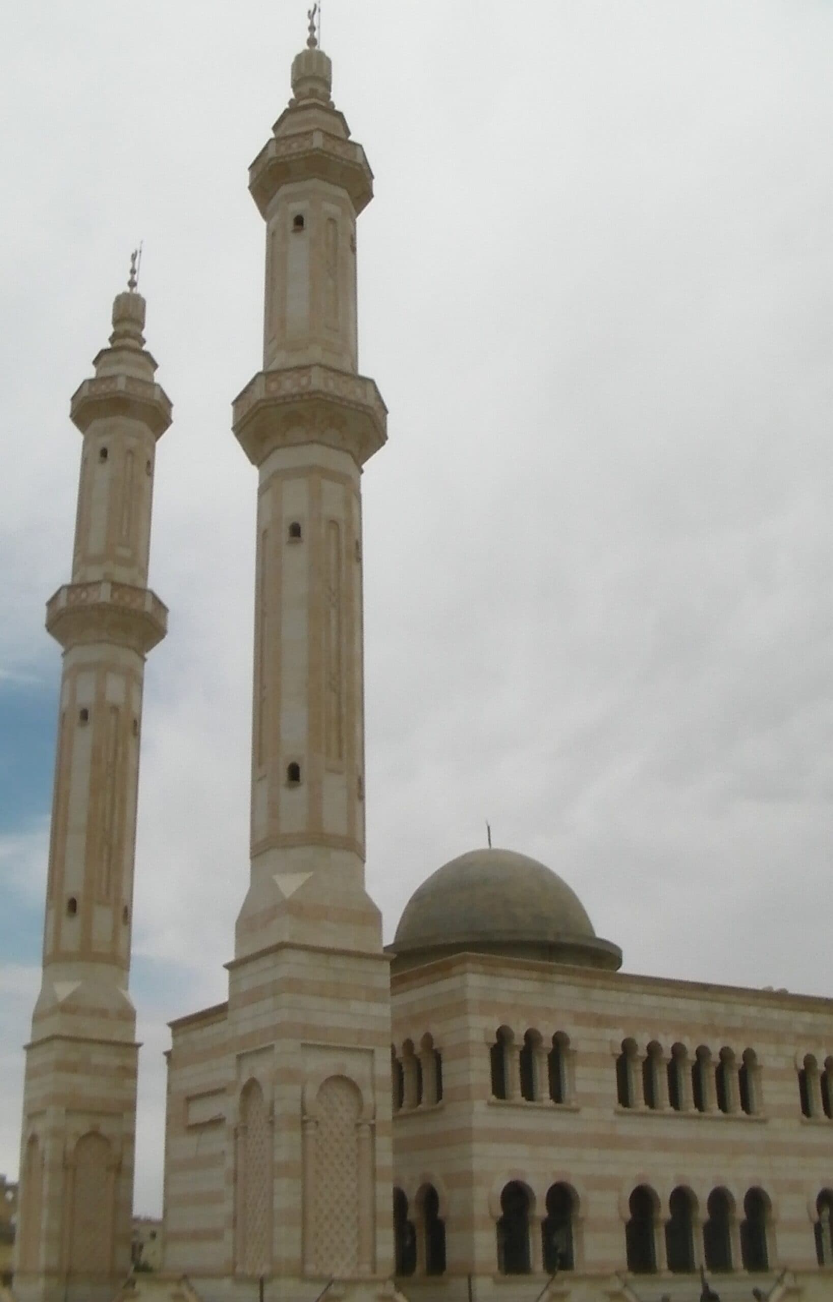 Azez'in kuzeydoğu çıkışında, Kilis yolundaki yeni cami: açık renk taş bantlı iki uzun minare, kurşun renkli kubbe ve kemerli pencere dizisi, bulutlu gökyüzü