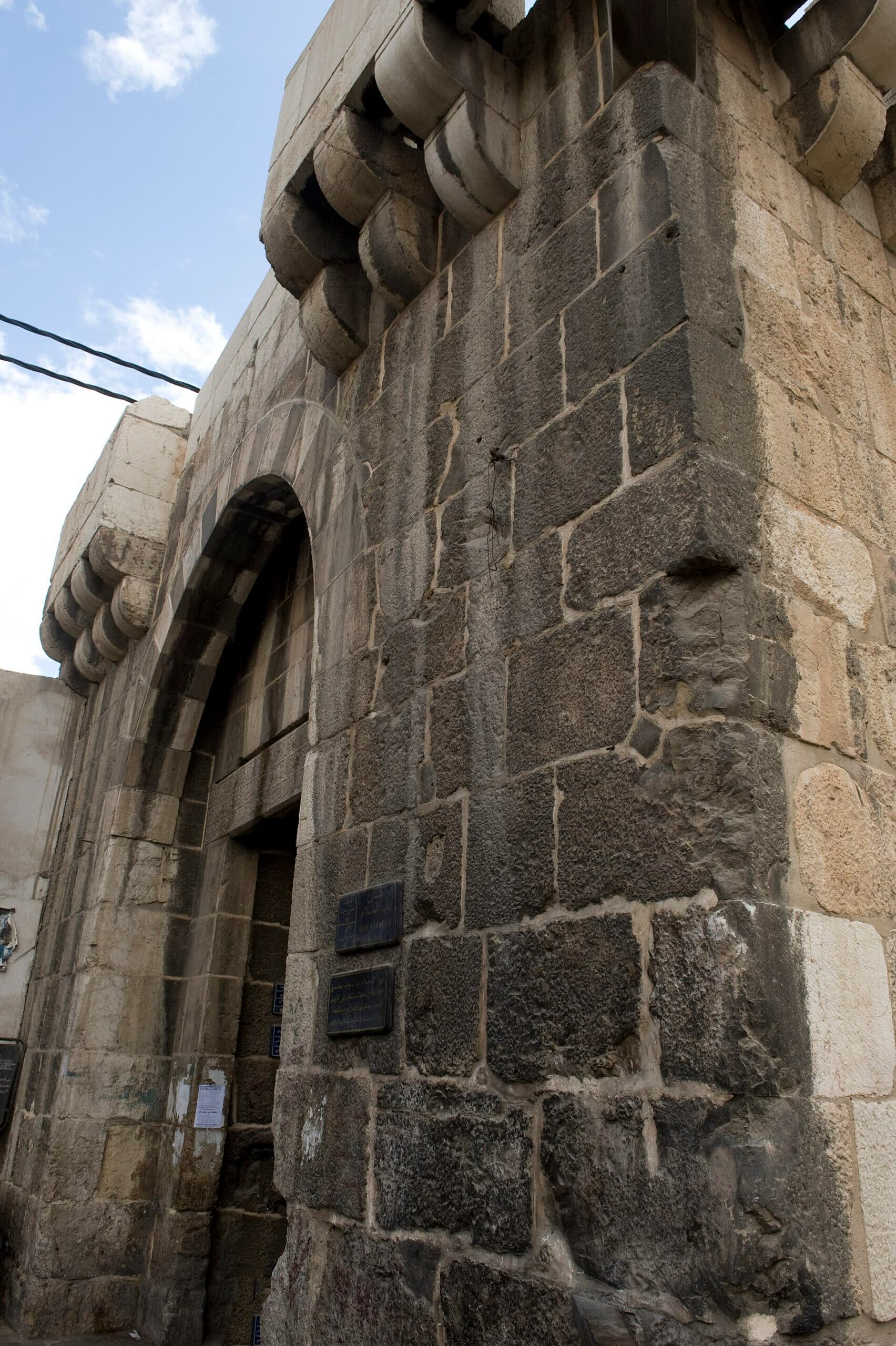 Bab el-Selam'ın taş kemeri, üstündeki mukarnas konsollar ve koyu bazaltla açık kireçtaşının karıştığı duvar, Şam