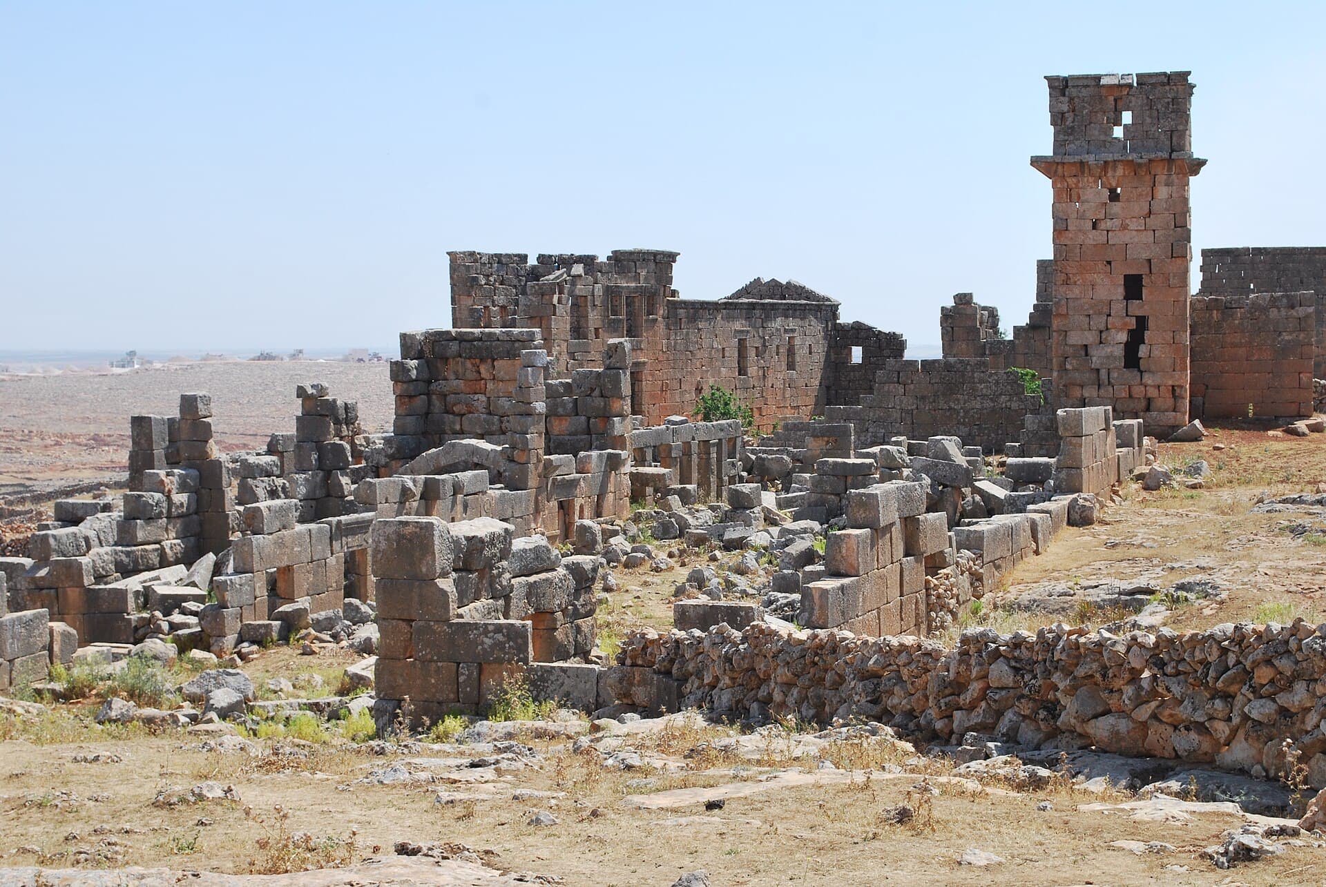Cerade'de kesme taş ev duvarları ve yıkıntı blokları arasında sağda yükselen çok katlı taş kule, arkada düzlük