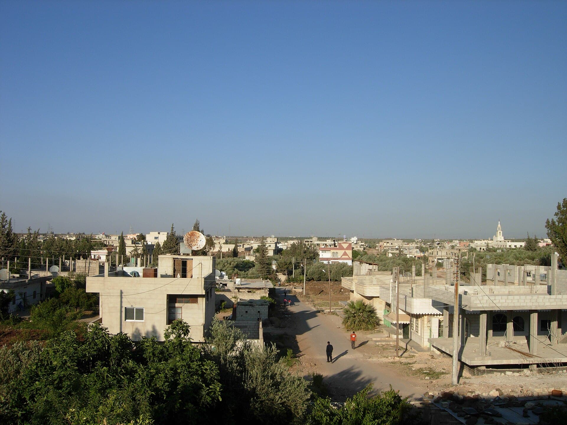 Deraa'da bir mahalle: düz damlı beton evler, aralarda zeytin ağaçları, uzakta minare