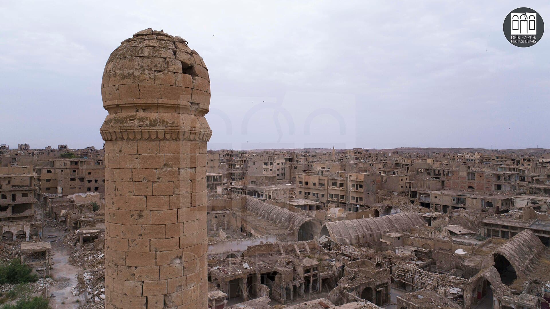 Deyrizor eski çarşılarının yüksekten görünümü: ön planda taş Ömerî minaresi, arkada tavanı çökmüş tonozlu çarşı sokakları ve hasarlı binalar, 2023