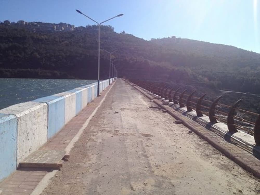 Düreykiş Barajı'nın kret yolu: solda baraj gölü, sağda demir korkuluklar ve aydınlatma direkleri, arkada ağaçlık yamaç