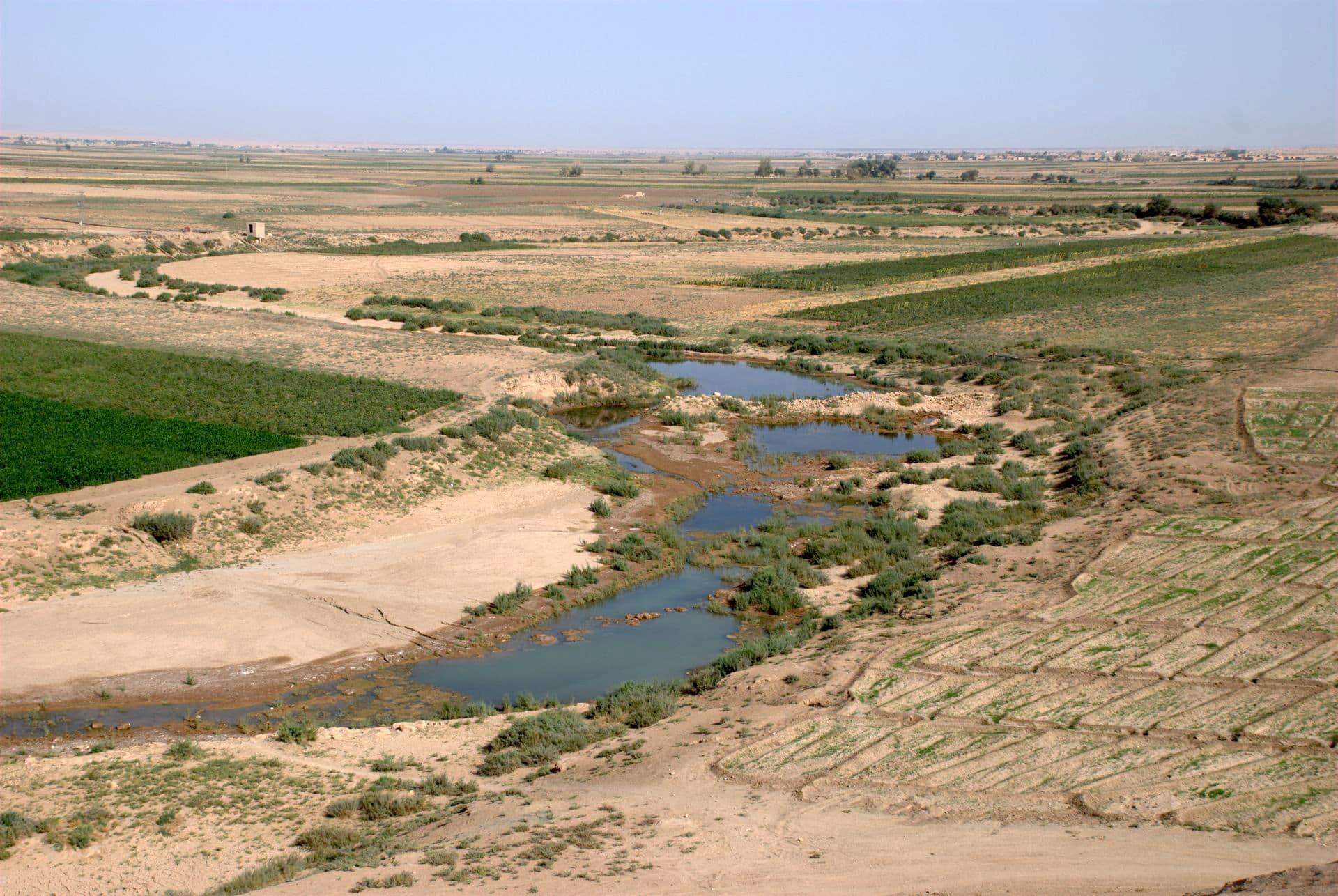 Tell Şeyh Hamad yakınında Habur Nehri: tarlaların arasındaki yatakta sığ göllere bölünmüş su, kıyıda çalılar ve arkada düz ova, Ekim 2009