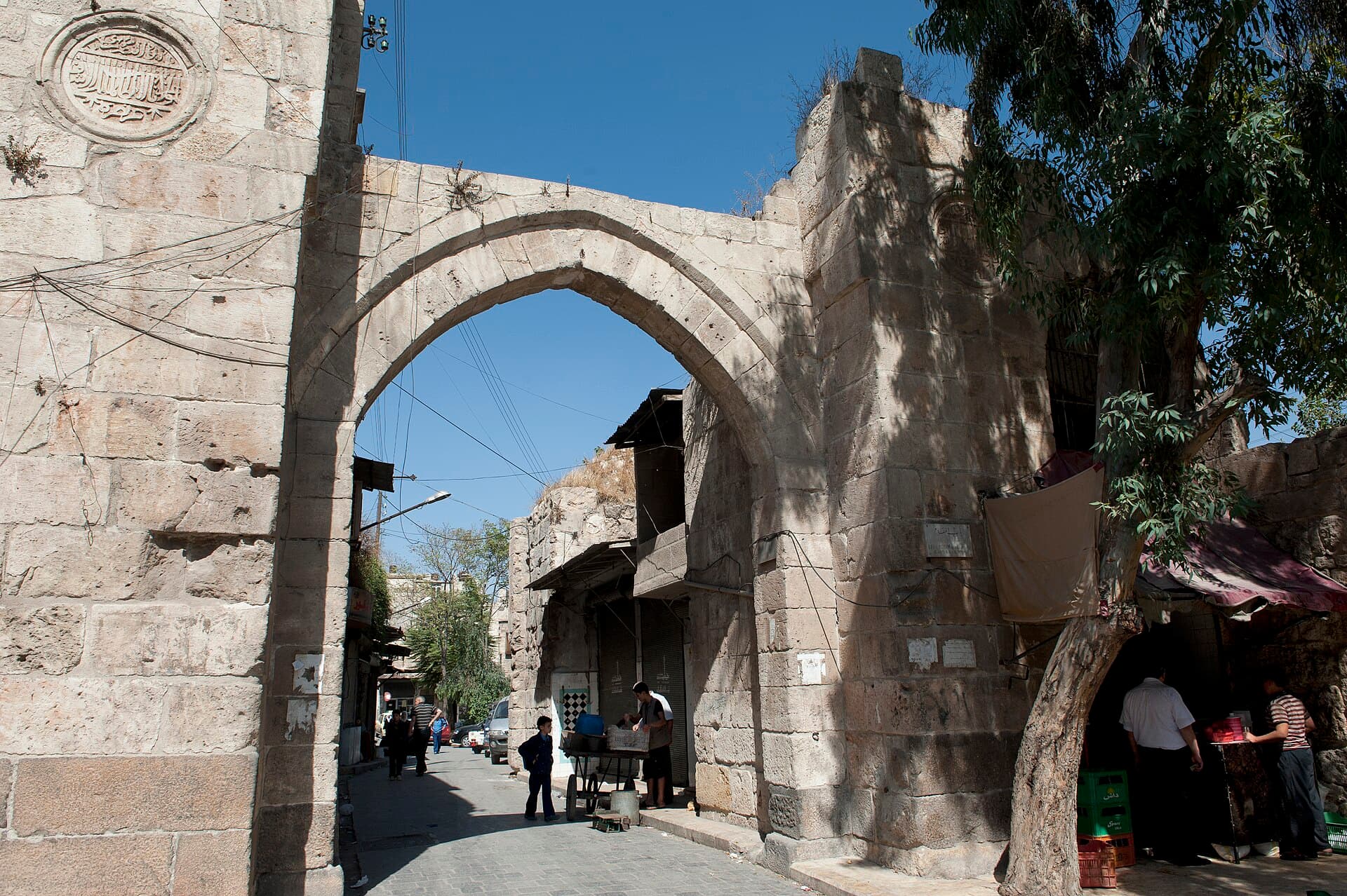 Bab el-Makam'ın sivri kemeri ve solundaki yuvarlak kitabe madalyonu; kemerin altından geçen sokak