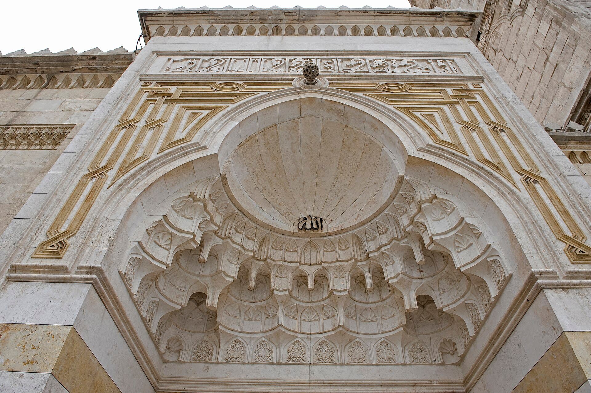Halep Ulu Camii'nin avluya açılan kapısı; kavsara mukarnas sıralarıyla dolu, üstünde yazı kuşağı ve geometrik örgü, altta açık-koyu taş şerit