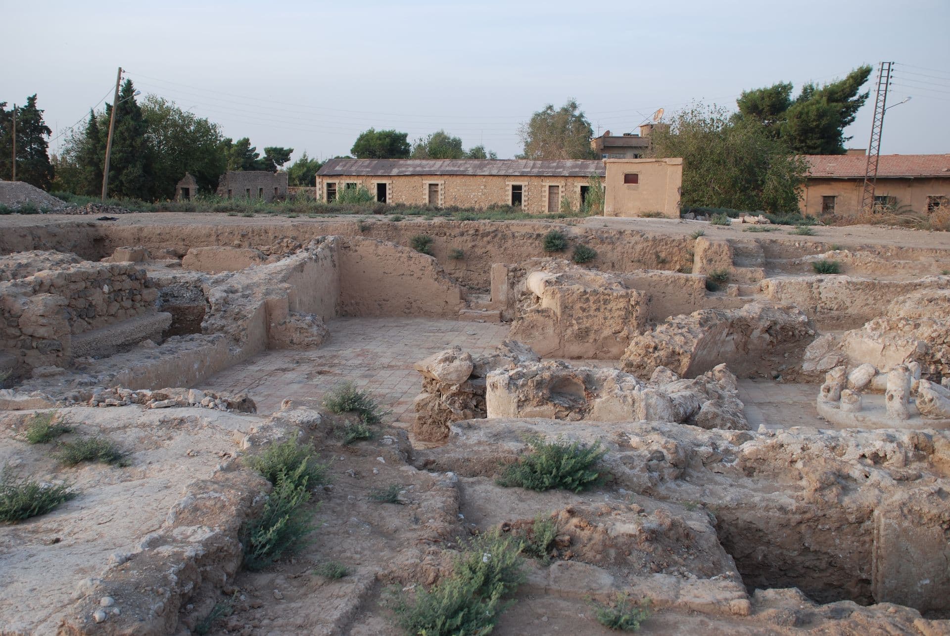 Haseke'nin ortasındaki höyükte açılmış kazı alanı; arkada Fransız mandası döneminden kalma taş yapılar