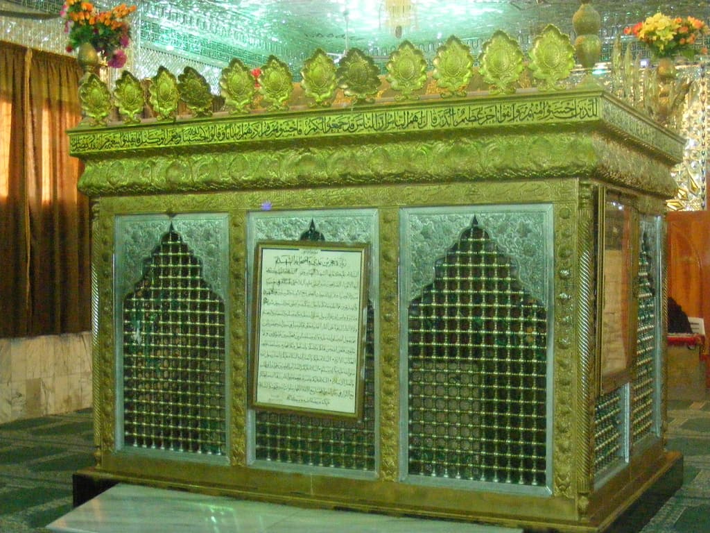 Adra'daki Hucr bin Adî türbesinde yeşil ve altın rengi kafesli sanduka, üstünde Kur'an ayeti kuşağı ve ziyaret duası levhası; 2007, tahribattan önce