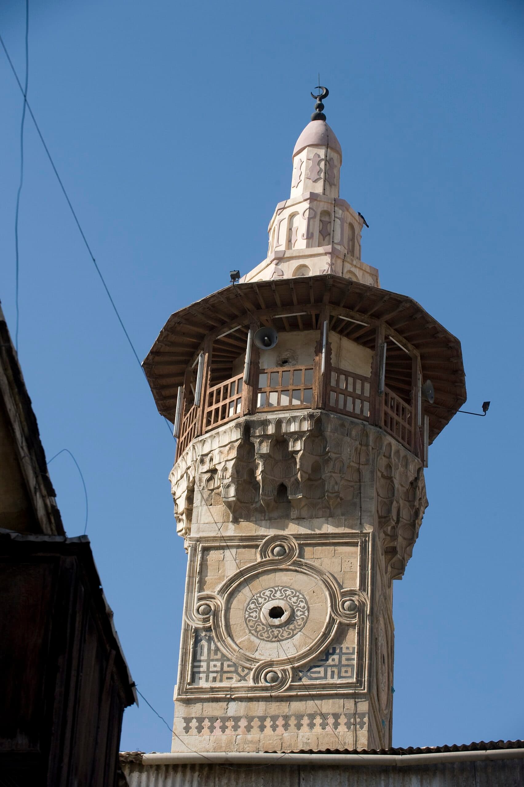Kalai Camii'nin kare gövdeli taş minaresi; gövdede oyma madalyon ve kûfî yazı şeridi, üstünde ahşap şerefe