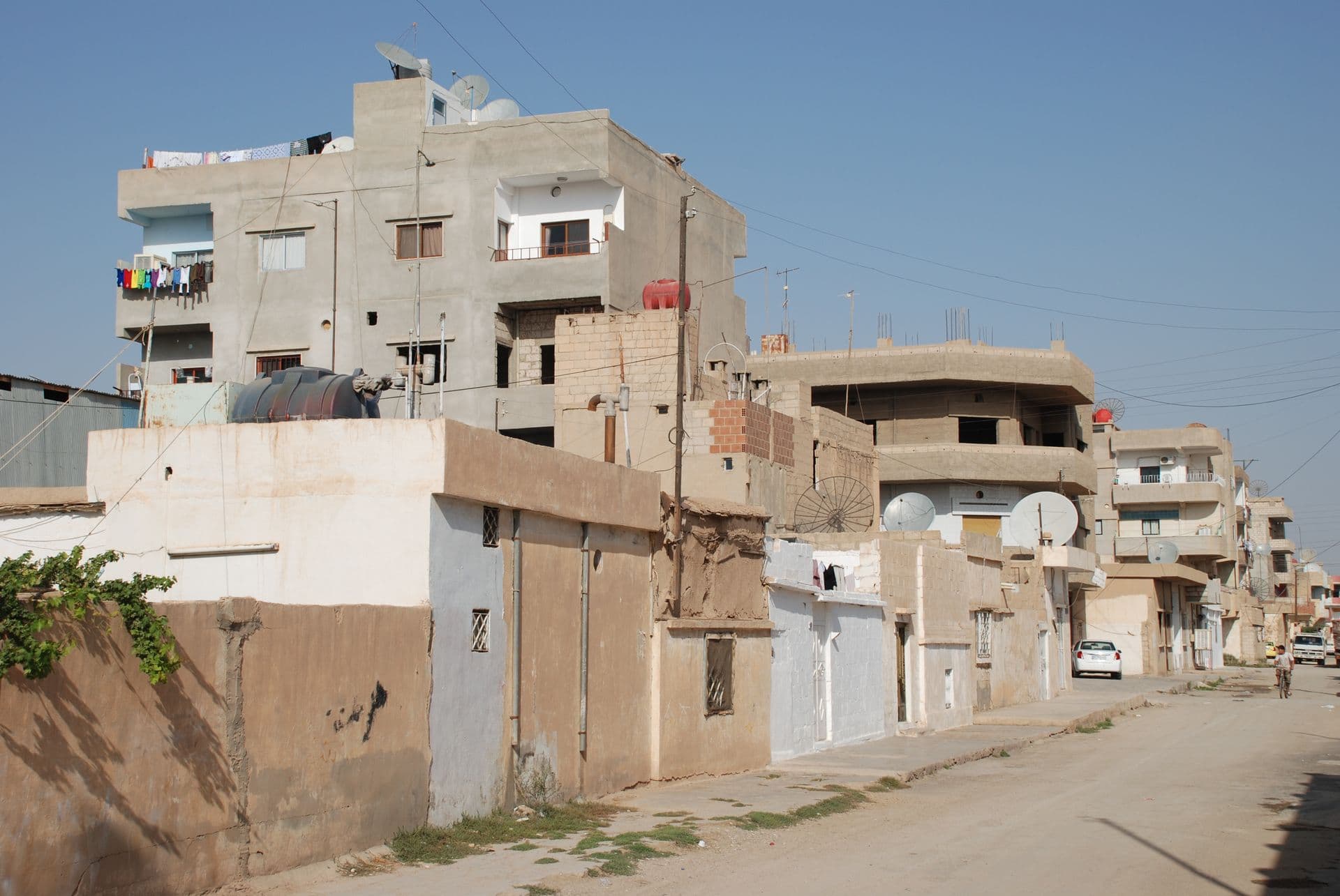 Kamışlı'nın doğu kesiminde, çatılarında çanak antenler olan çok katlı beton evlerin sıralandığı toprak kenarlı bir sokak, 2009