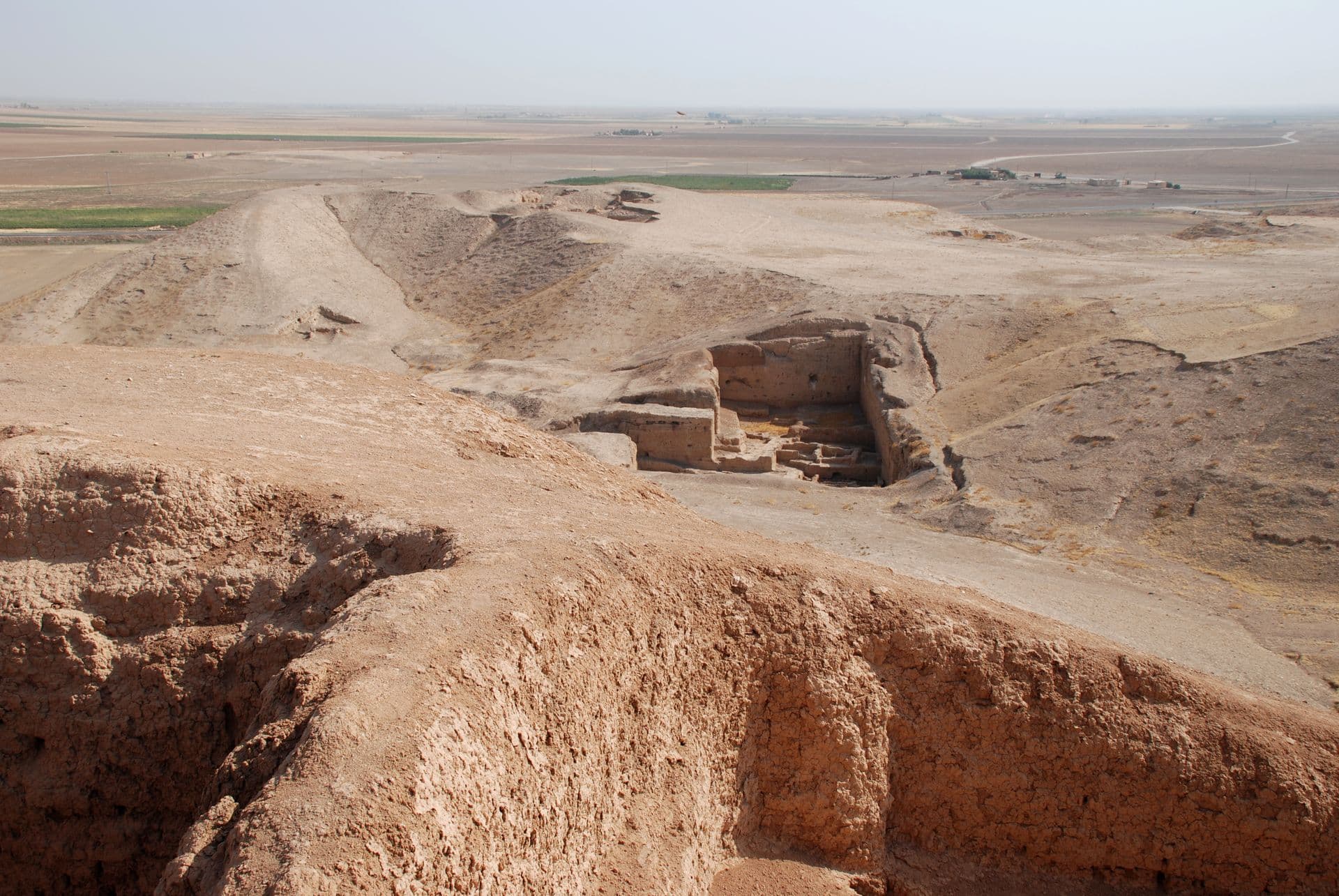 Tell Brak höyüğünün tepesinden kerpiç duvarlı bir kazı açması ve arkada uzanan düz Yukarı Habur ovası