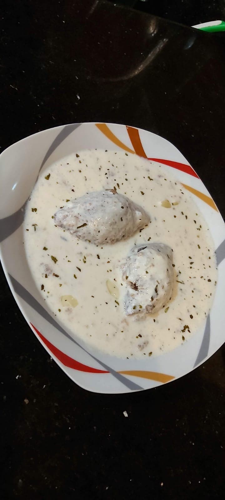 Beyaz tabakta kurutulmuş nane serpilmiş yoğurt sosunun içinde iki kibbe köftesi