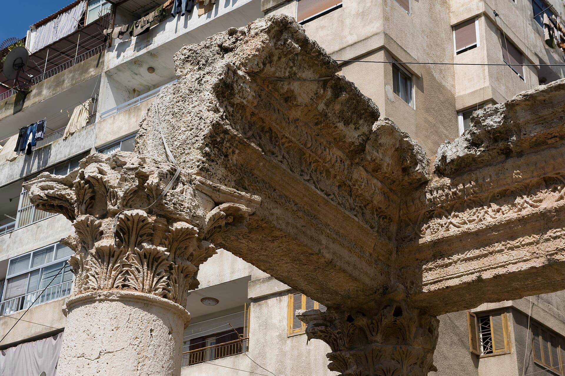 Lazkiye'nin Suleybe mahallesinde Bacchus Sütunları'nın Korint başlıkları ve oymalı taş kirişi, arkada apartman cepheleri