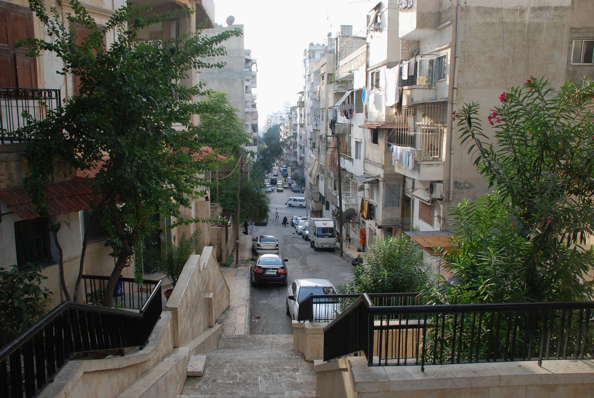 Lazkiye şehir merkezinde apartmanların arasına inen merdivenli yaya geçidi ve ağaçlı dar cadde