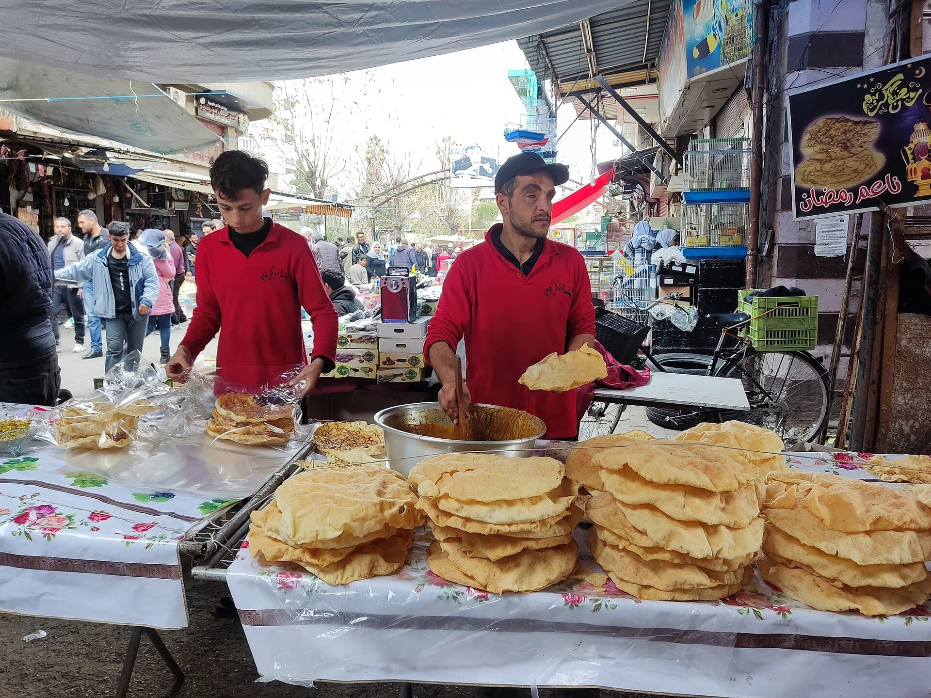 Şam'da Ramazan tezgâhında üst üste yığılmış naim ekmekleri ve kızartan iki satıcı