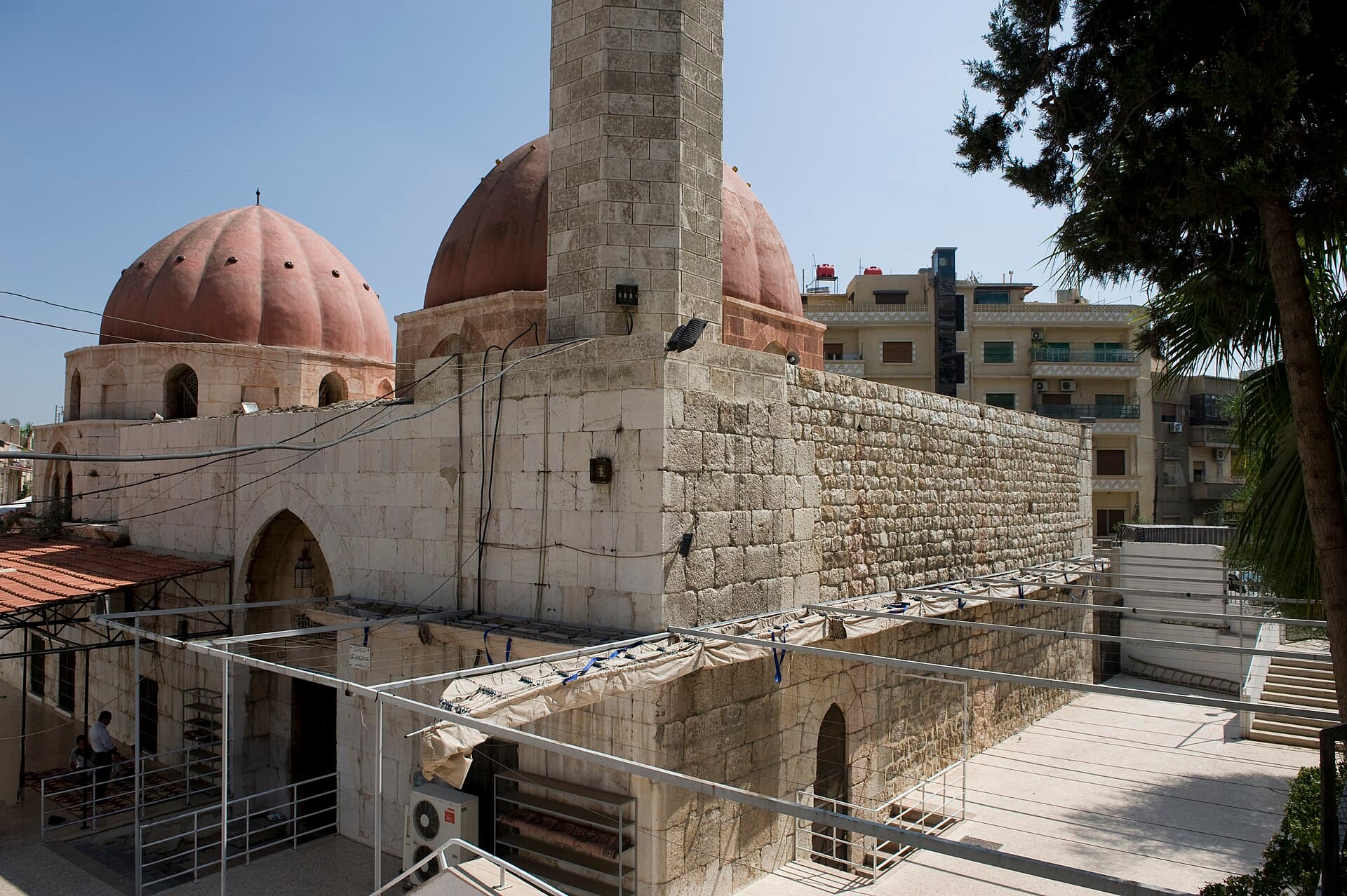 Rükniye Medresesi'nin dilimli kırmızı kubbeleri ve kare minaresi, arkada Rükneddin semtinin apartmanları, Şam