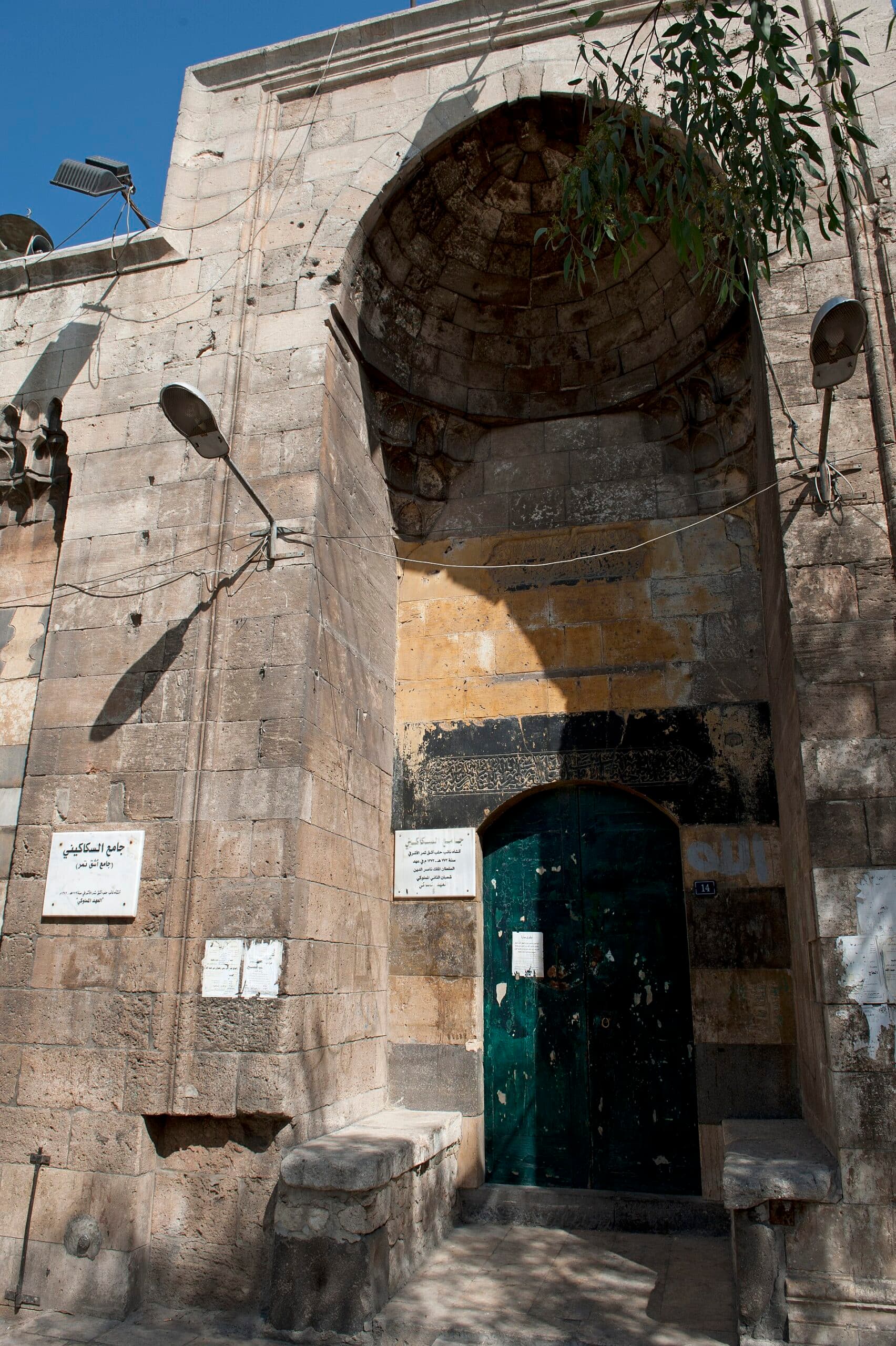 Sekakini Camii'nin sokağa bakan taş taçkapısı; derin nişin üstünde mukarnaslı yarım kubbe, yeşil ahşap kapının iki yanında levhalar