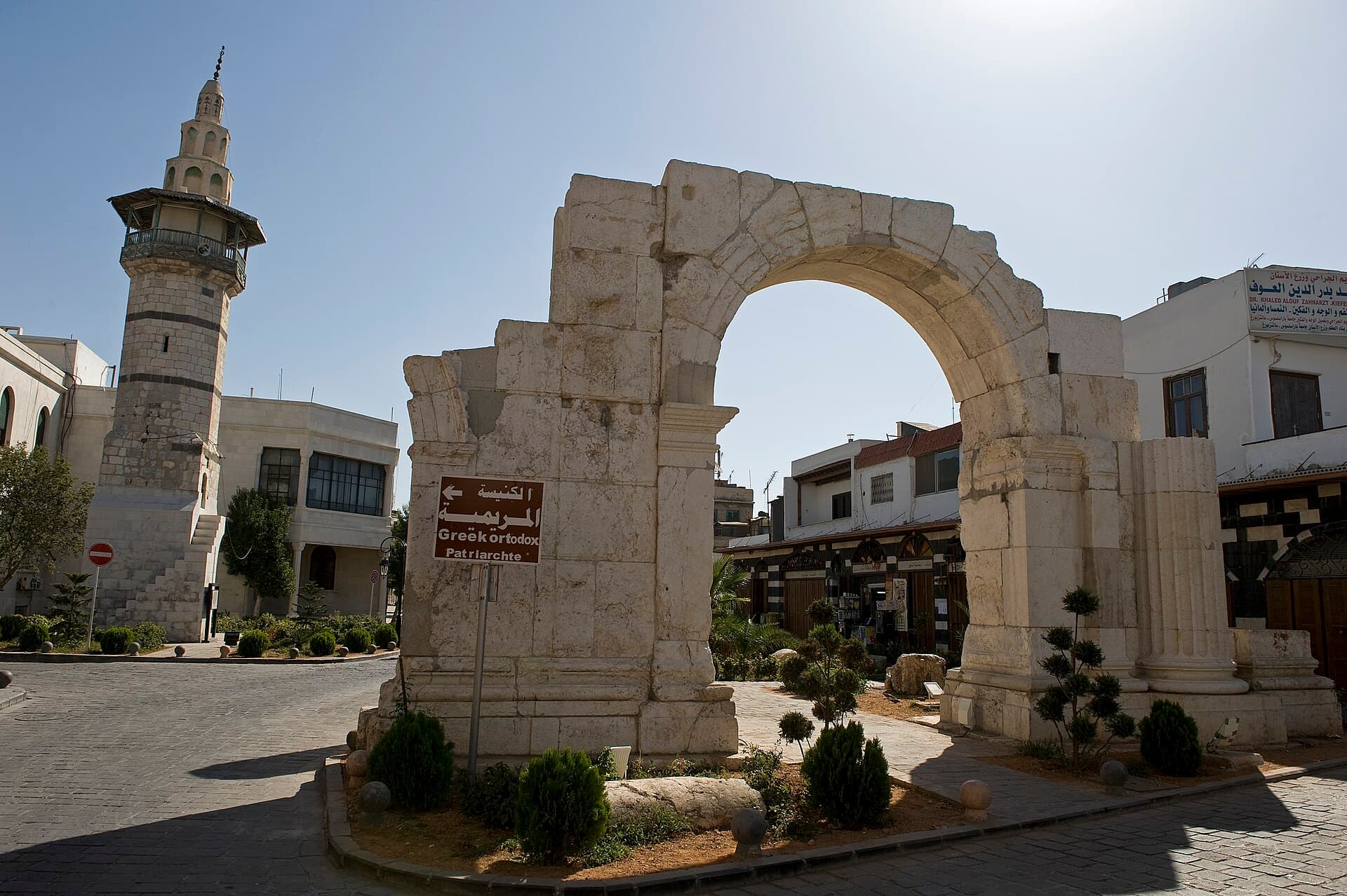 Şam eski şehrinde Doğru Sokak'taki Roma takı; önündeki kahverengi tabela Meryem Ana Katedrali'nin yönünü gösteriyor, solda taş gövdeli bir cami minaresi