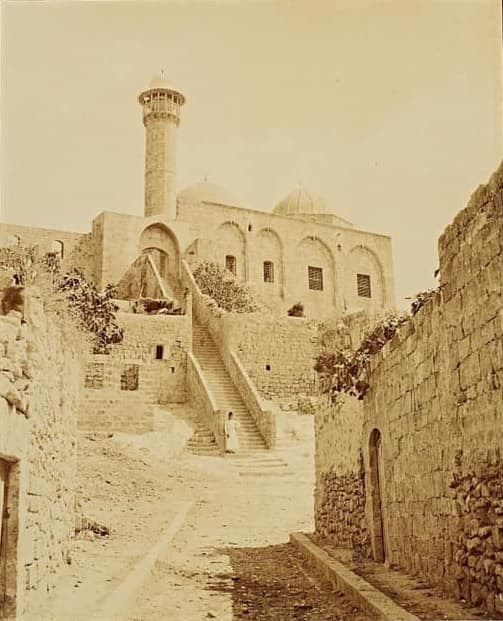 1875 tarihli fotoğrafta Lazkiye'de Şeyh Mağribî Camii: taş sokaktan yukarı çıkan uzun merdiven, arkada kubbeleri ve minaresiyle cami