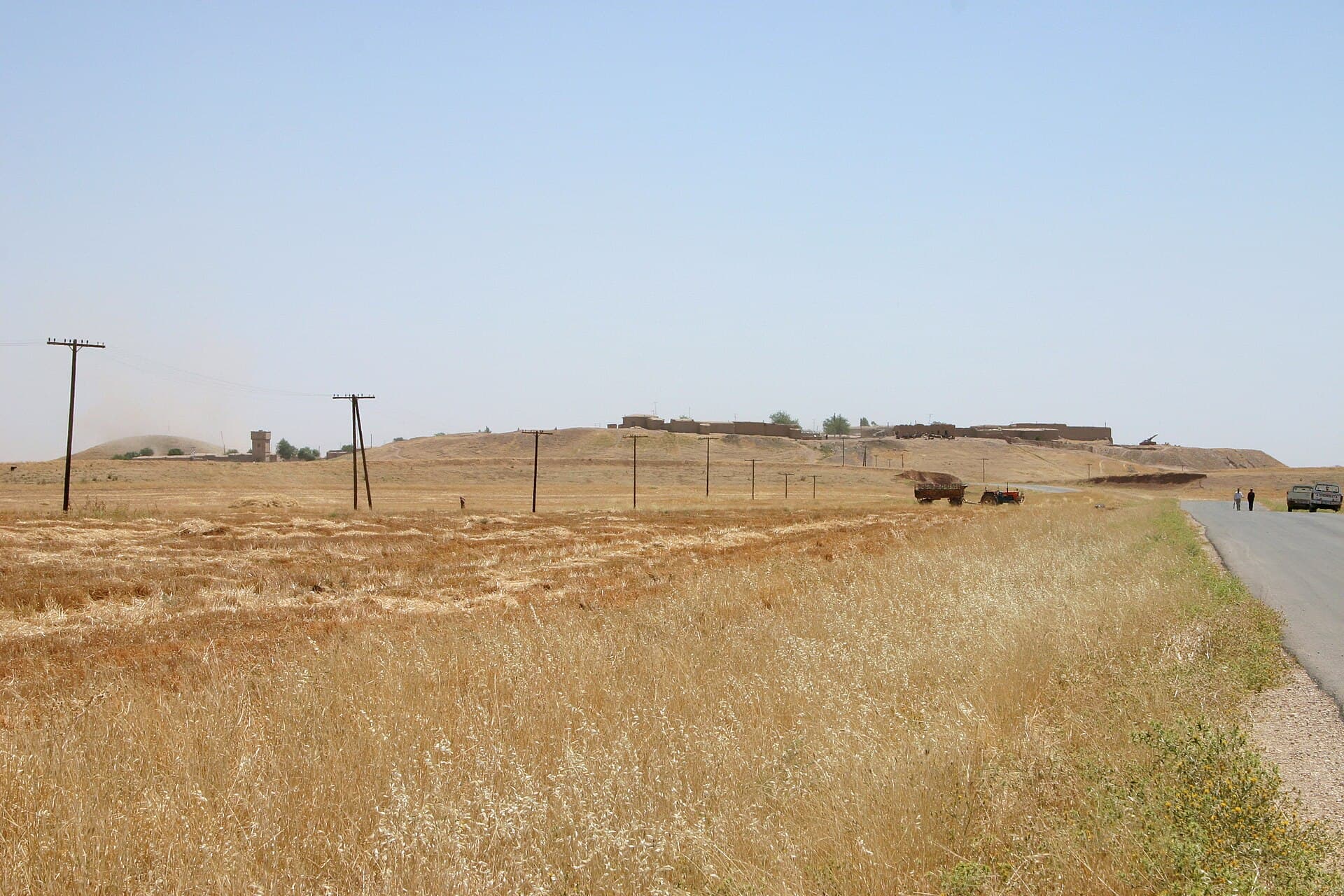 Tell Leilan höyüğü; üstünde bugünkü köyün evleri, önünde biçilmiş tarlalar ve asfalt yol