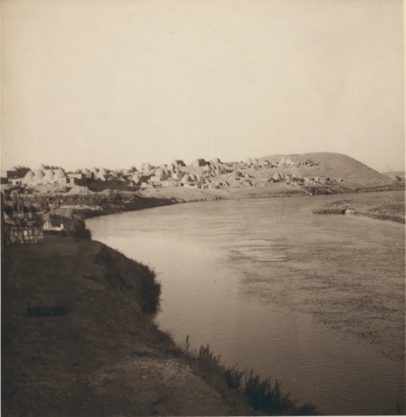 1939'da Tel Temir: önde Habur Nehri'nin kıvrımı, karşı kıyıda kubbeli kerpiç evler ve arkada höyük; siyah-beyaz fotoğraf