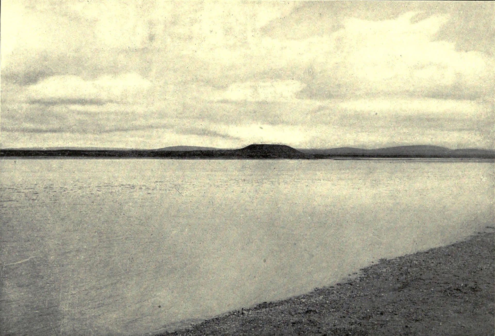 Fırat'ın karşı yakasından görülen Tell Ahmar höyüğü: durgun ırmağın ardında ovada tek başına yükselen koyu bir tepe; 1910 tarihli siyah-beyaz fotoğraf