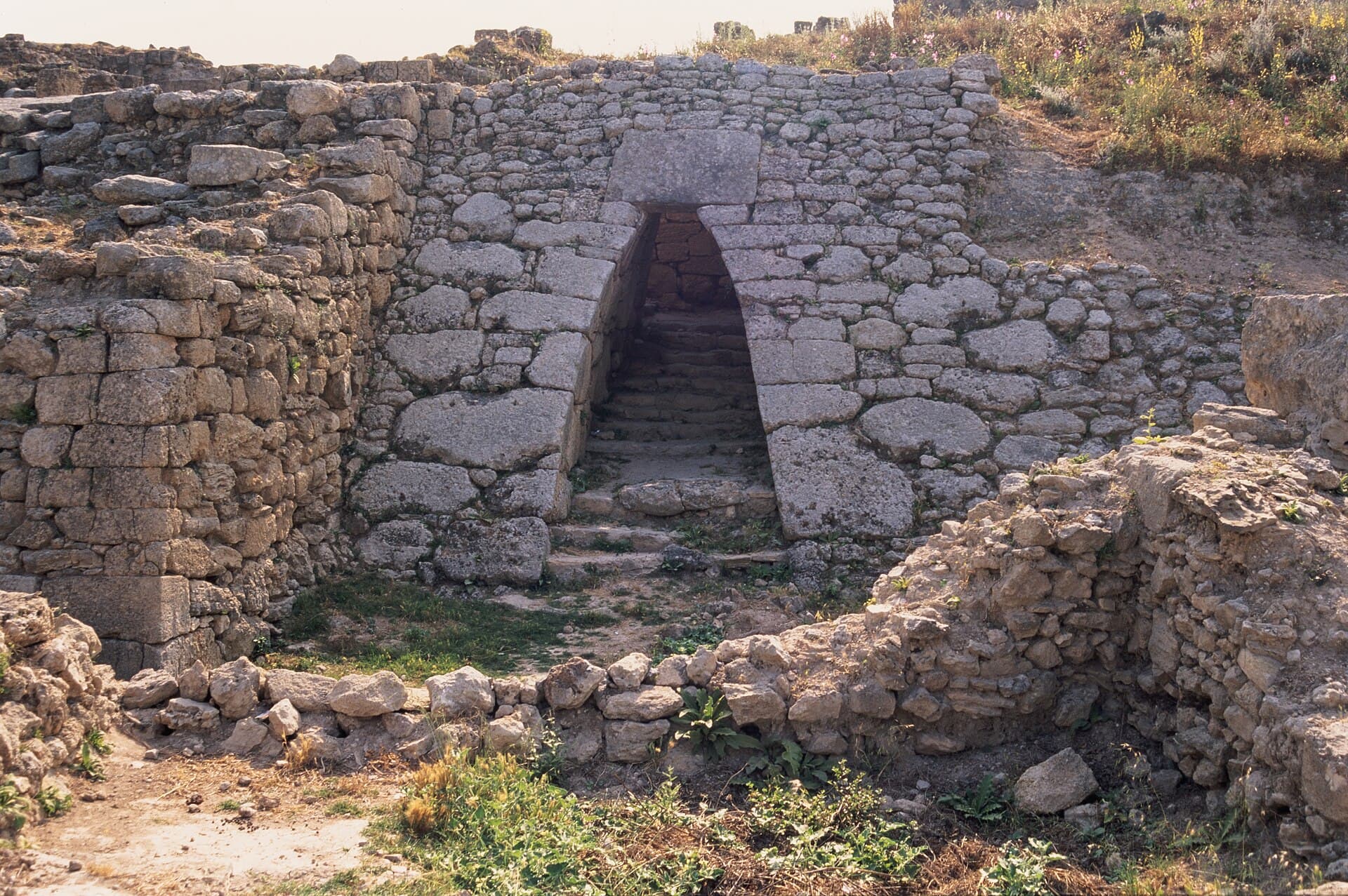 Ugarit höyüğünde iri taşlarla örülmüş sur duvarının içinden geçen, basamaklı, dar ve sivri tonozlu antik kapı