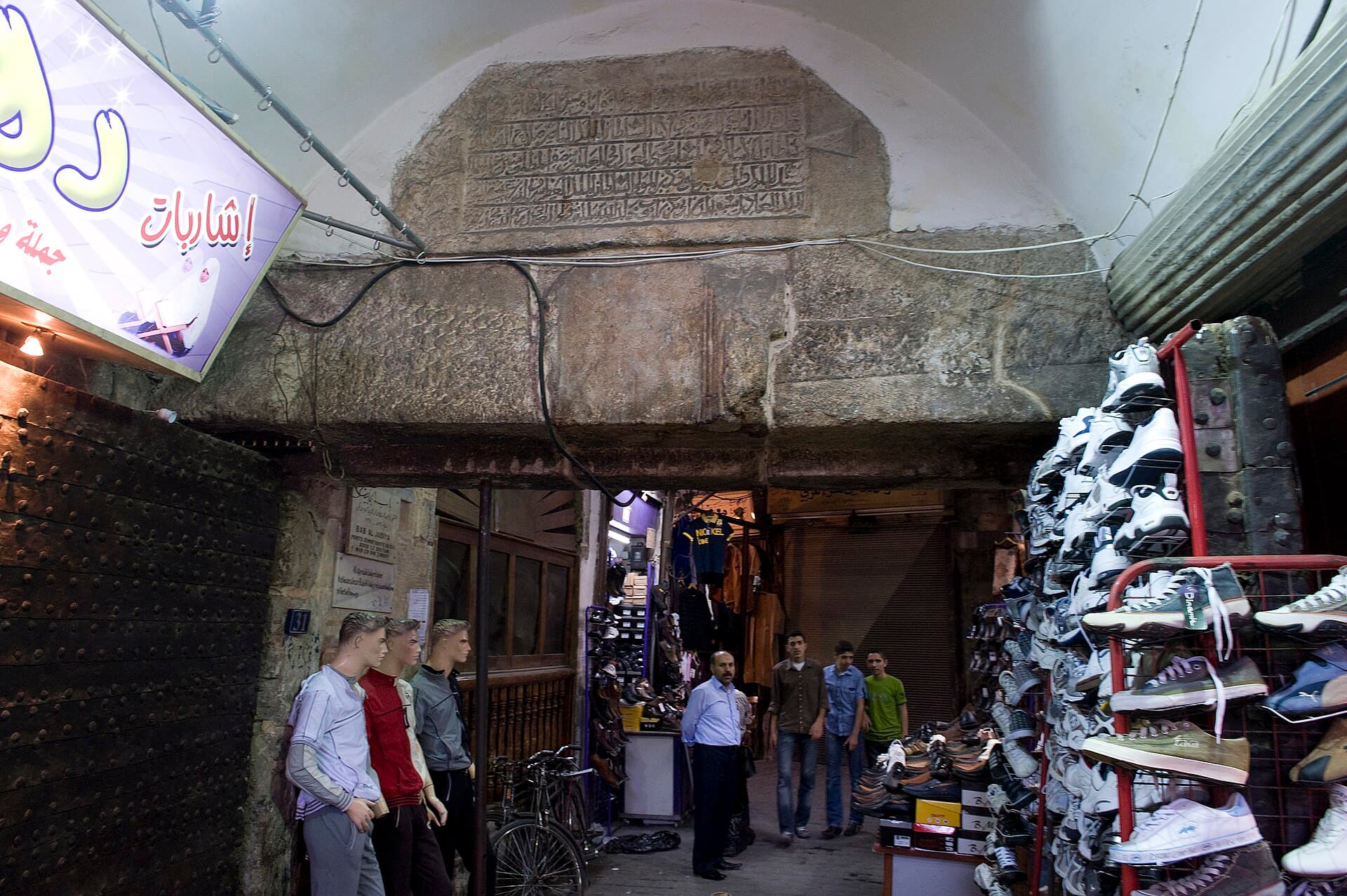 Bab el-Cabiye'nin taş lentosu ve üstündeki kitabe levhası; geçidin iki yanında ayakkabı tezgâhları