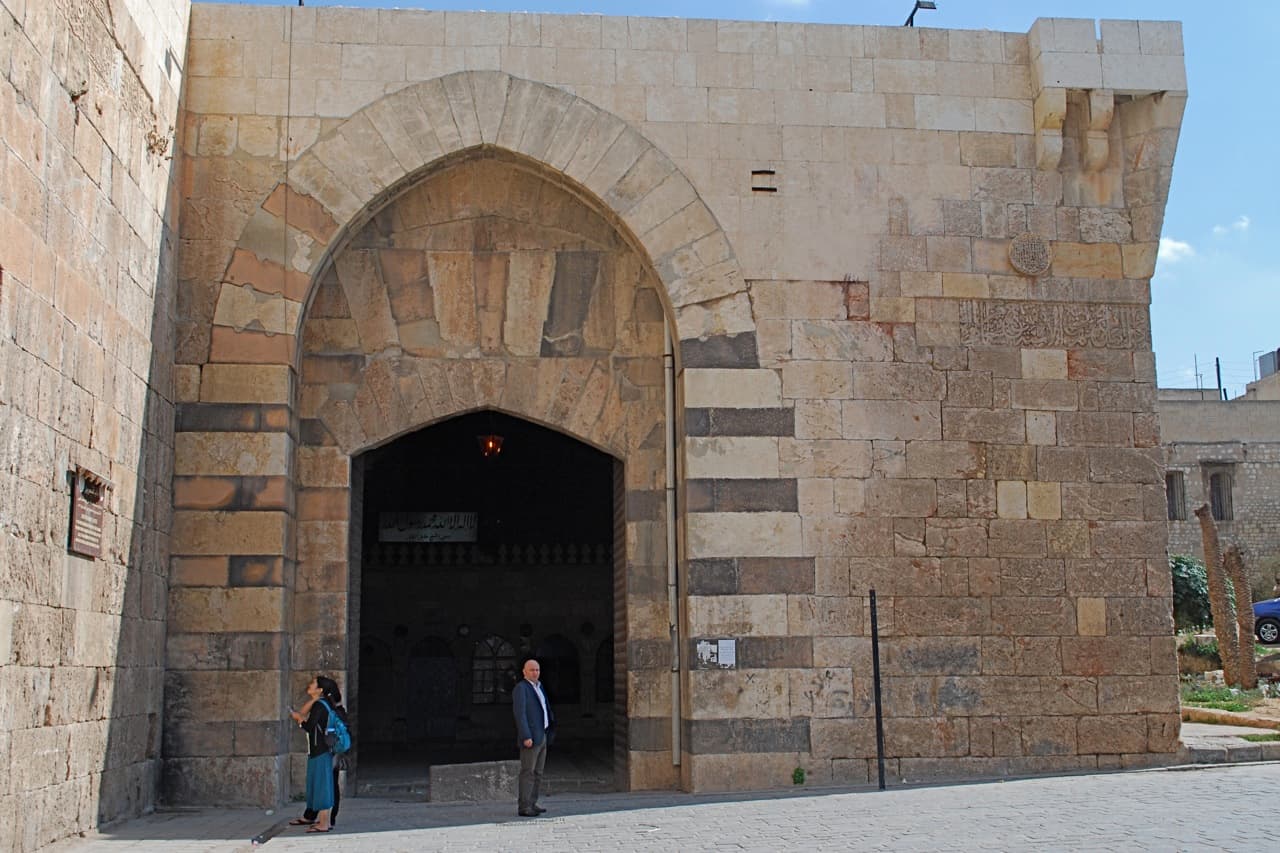 Bab Kınnesrin'in sivri kemerli taş cephesi; sağ yanda açık ve koyu taş sıraları, ortada geçidin karanlığı