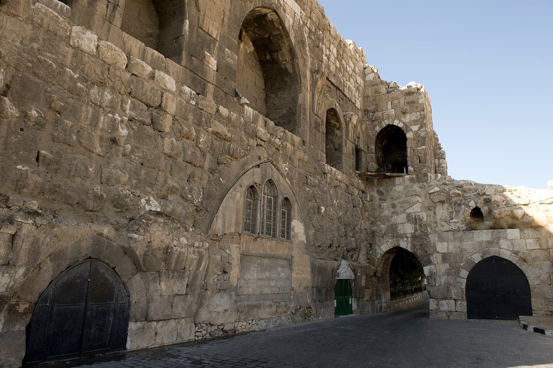 Şam Kalesi'nin kuzey duvarı boyunca uzanan taş döşeli sokak; duvardaki sivri kemerli üçlü pencere Ebu'd-Derda Camii'nin, arkadaki kemerli geçit Bab el-Hadid kapısının