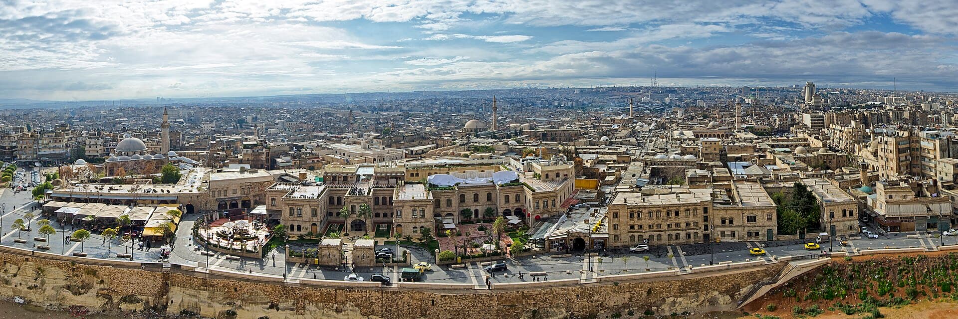 Halep eski şehrinin kale surundan panoraması: önde kale hendeği ve meydan, arkada minareler, kubbeler ve düz damlar