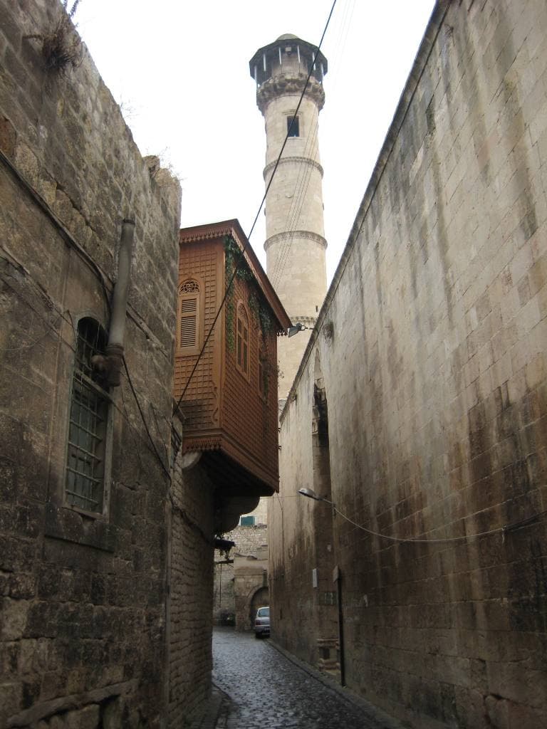 Rumi Camii'nin minaresi dar bir Halep sokağının ucunda; solda ahşap cumba, iki yanda taş duvarlar