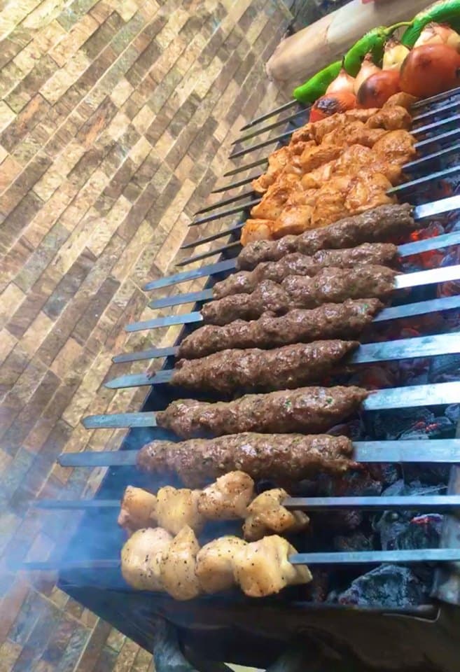 Kömür ateşinin üstünde sıra sıra kebap şişleri, tavuk parçaları ve közlenen domates, soğan, yeşil biber