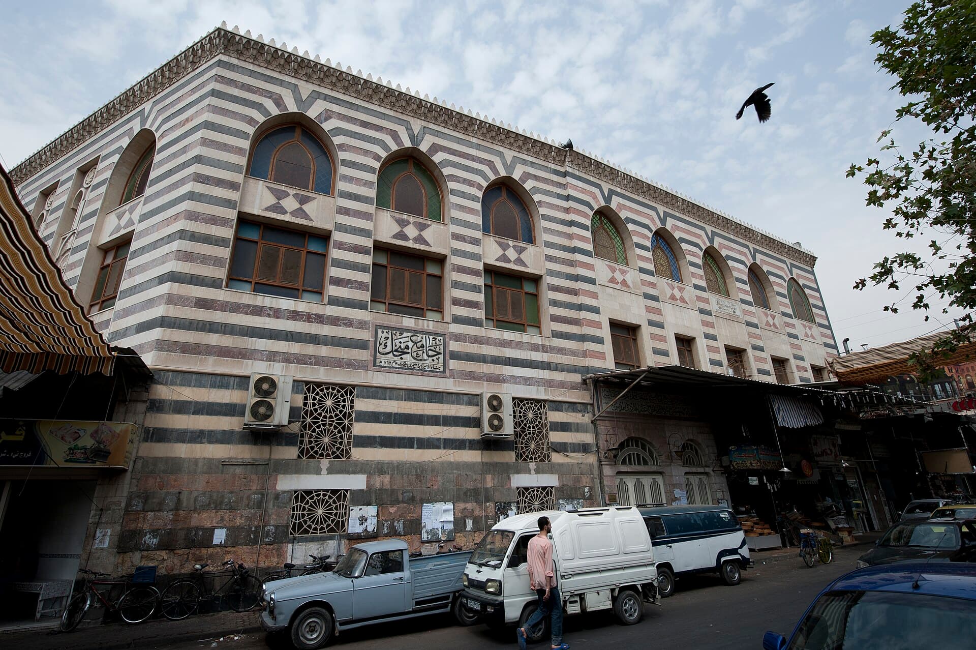 Mencik Camii'nin şeritli taş cephesi; alt katta çarşı dükkânları, üst katta sivri kemerli pencereler