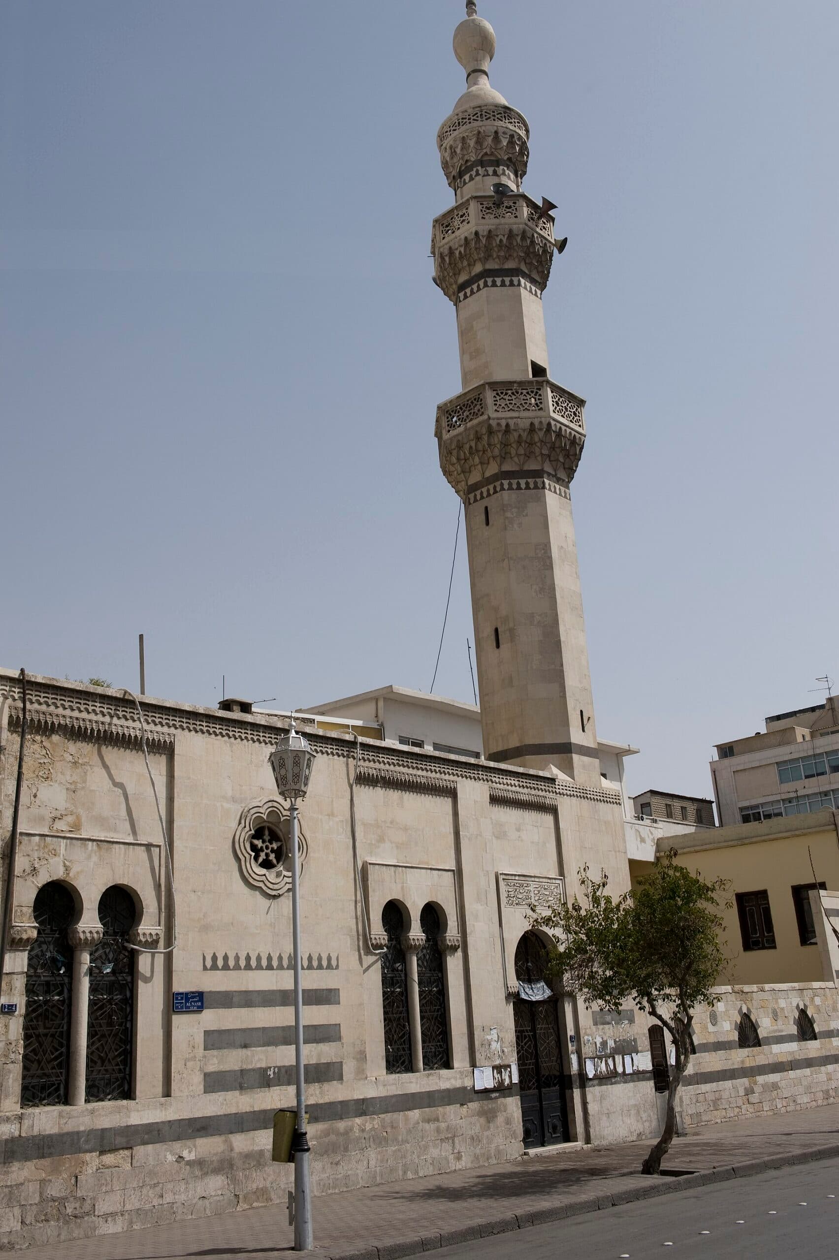 Şam'daki Mevlevi Tekkesi ve Camii: Nasr Caddesi'nden cephe, alt sıralarda almaşık taş örgü, ikili kemerli pencereler ve iki mukarnaslı şerefeli sekizgen minare